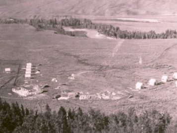 A black-and-white aerial photograph of small, discrete buildings under construction next to existing structures.